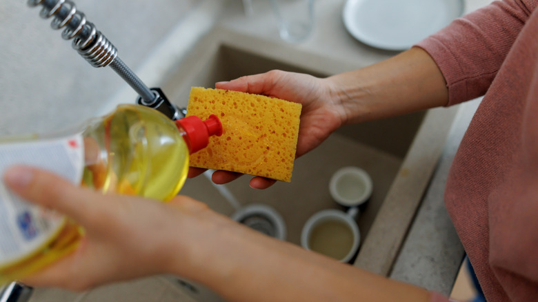 Woman applying dish soap to sponge over kitchen sink
